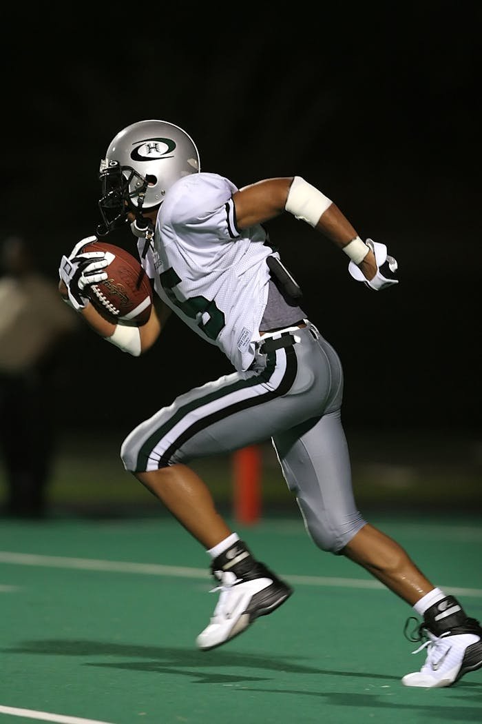 service-03 High-speed capture of a football player running on the field during a night game, showcasing athleticism.