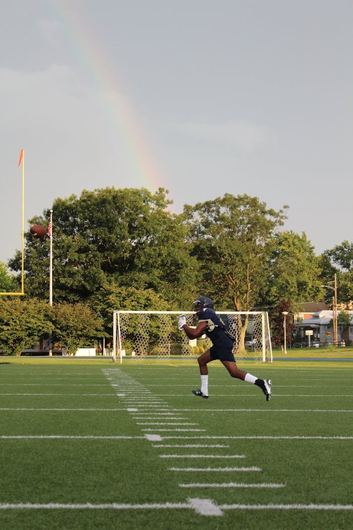 about-img Athlete catching a pass on a football field with a rainbow in the background.
