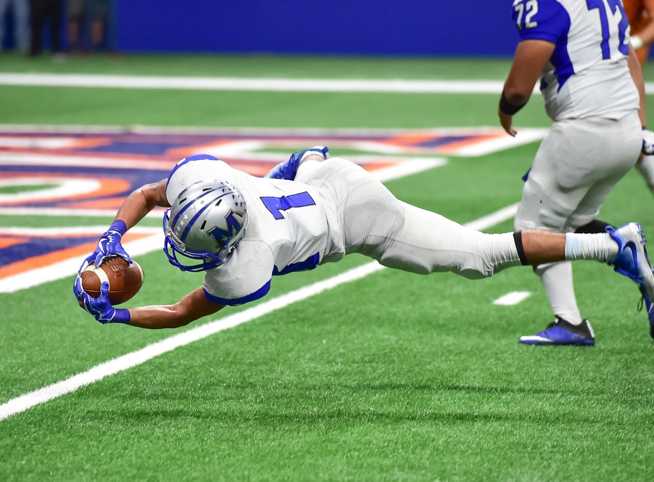 about-me-img Football player making an incredible diving catch during a high-energy game in the stadium.