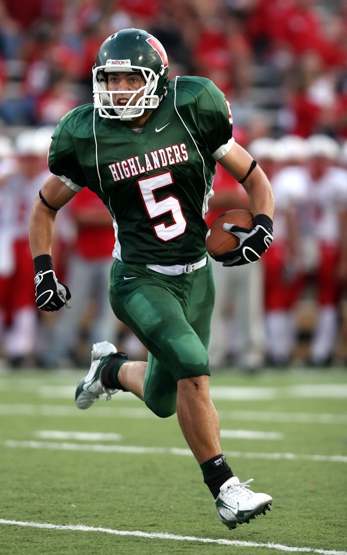 services-img High school football player in green uniform running with the ball during a game.