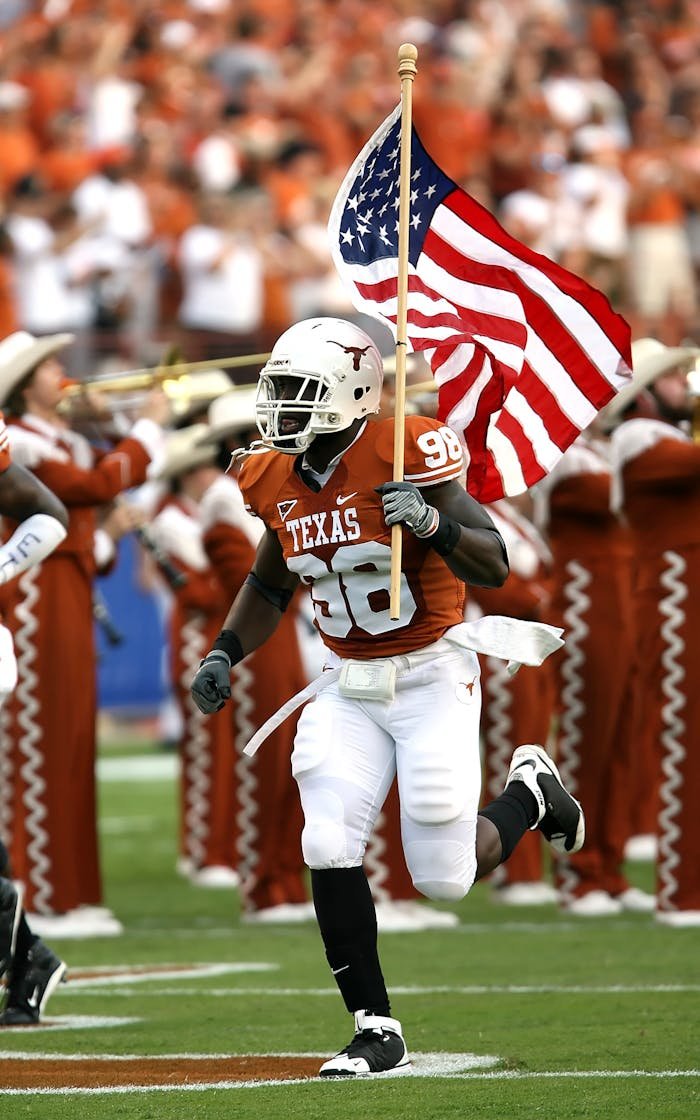 services-01 Football player runs with American flag at a Texas game, showcasing team spirit and national pride.