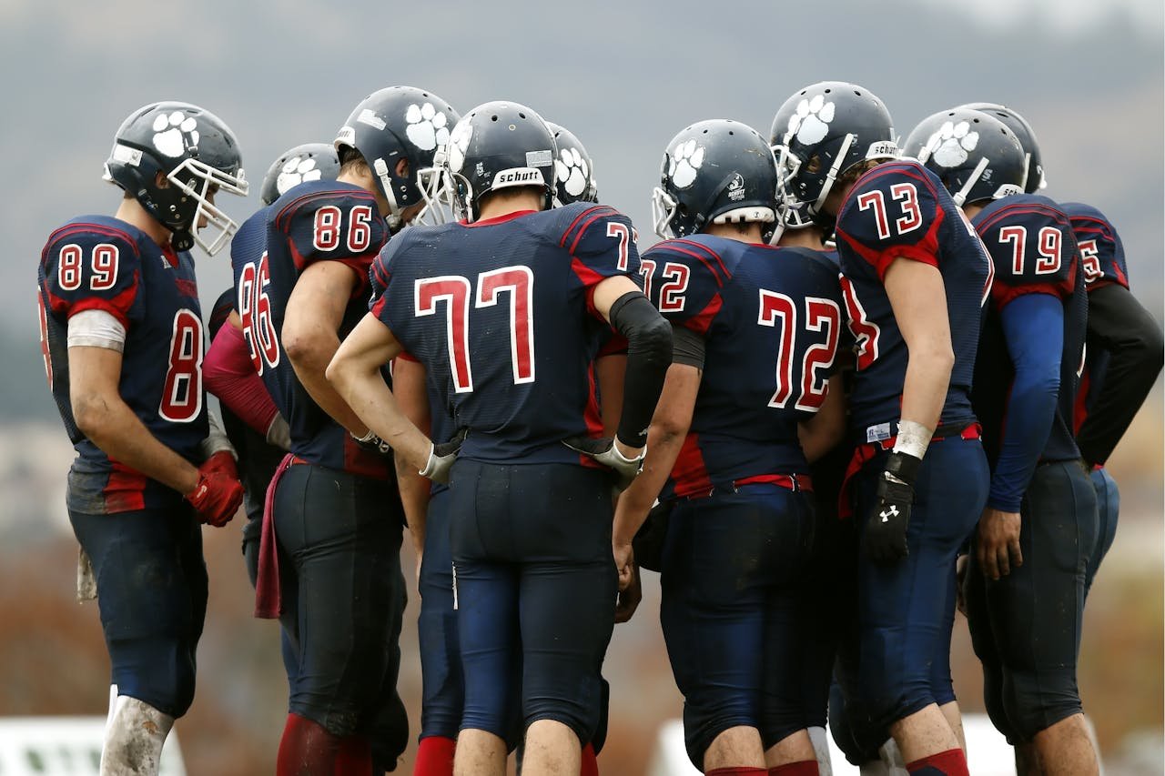 why-choose-me American football players in a huddle planning their next move on a grassy field.